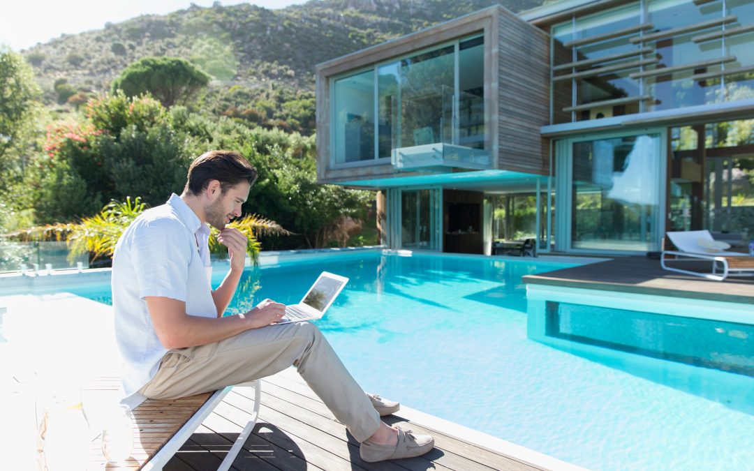 Young man using laptop at sunny luxury poolside
